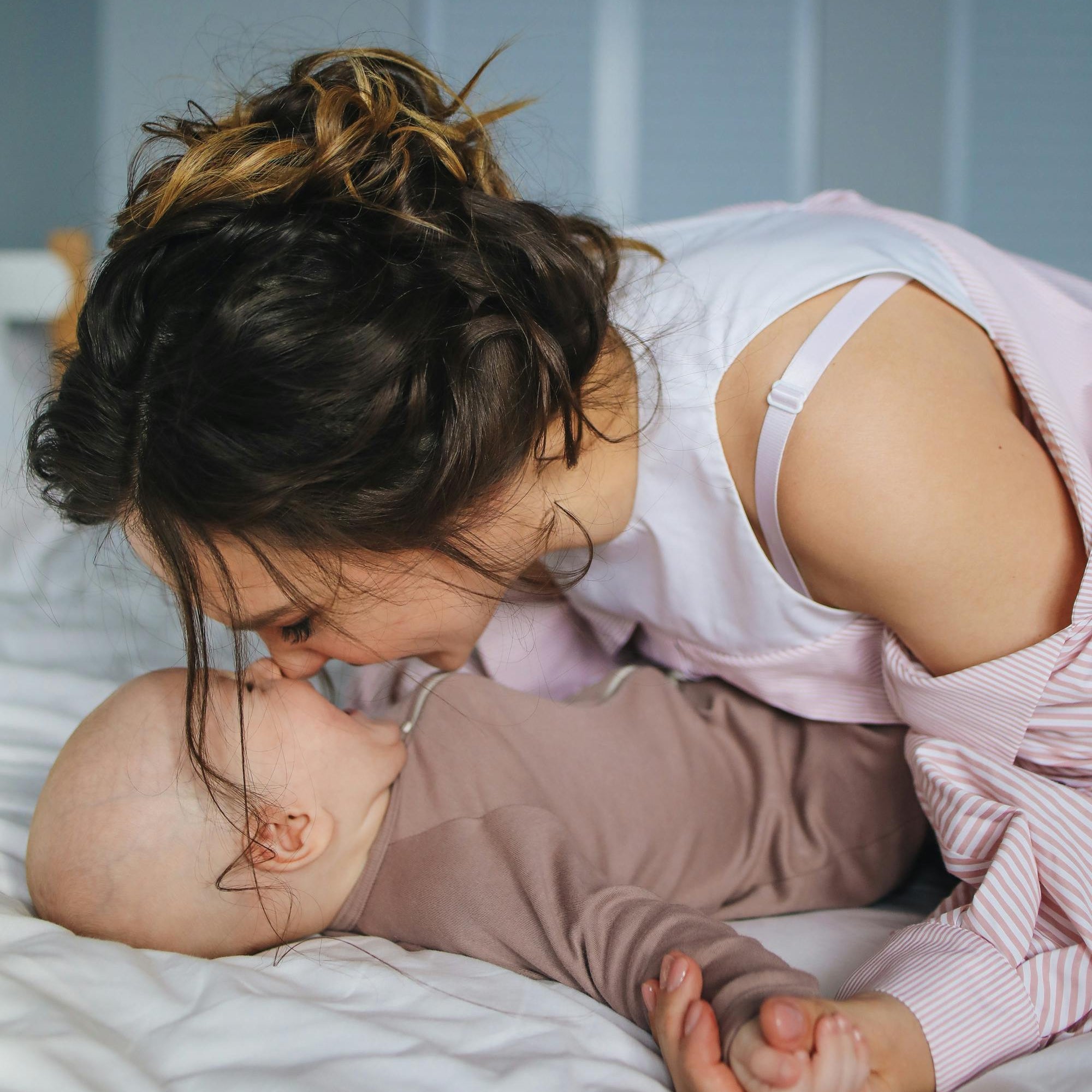 Woman and baby lying on a bed, with woman leaning over baby